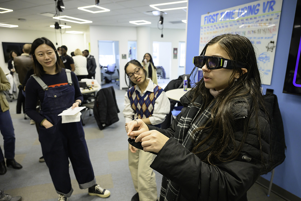 A student wears VR glasses while a professor and another student look on.