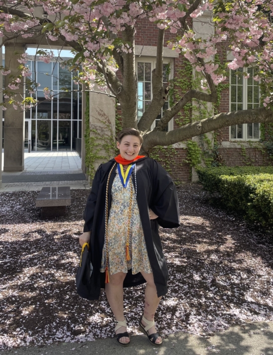 student in cap and gown under flowering tree