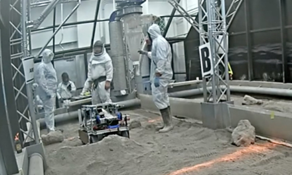 (l to r): Francesca Daszak, a NASA Lunabotics official, and Rachael He approach the Rochester team’s automated mining robot in the competition arena at Kennedy Space Center. (Image from NASA livestream of Lunabotics MMXXII)