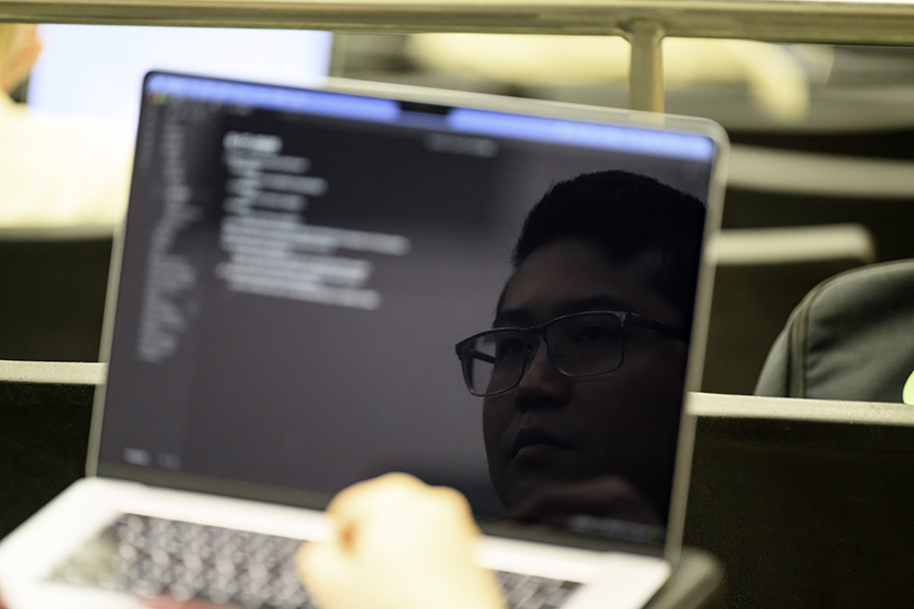 A face shown in silhouette on a laptop screen of code.