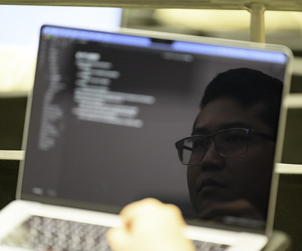 A laptop screen with code reflects the face of the user.